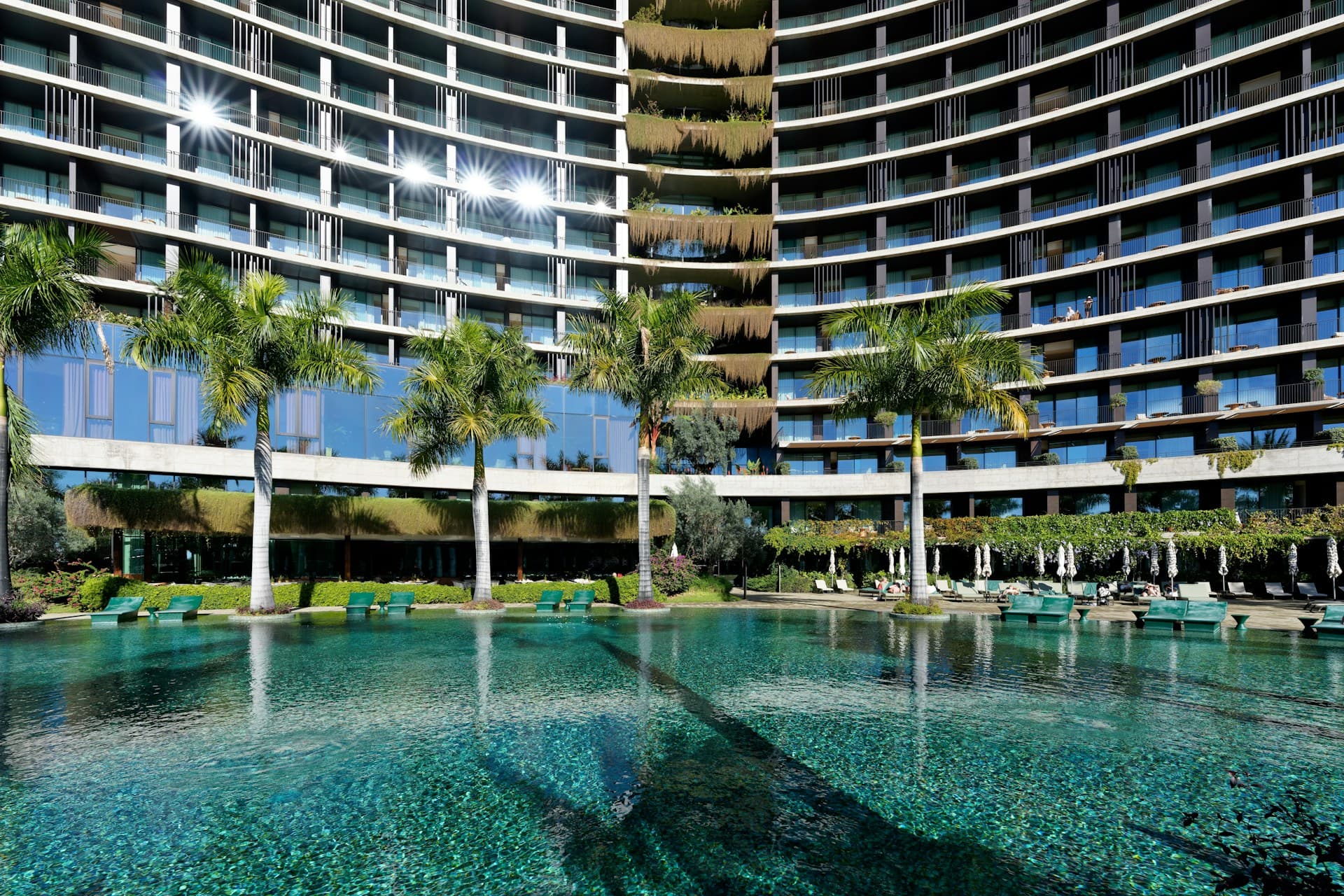 Luxury resort hotel exterior with a large outdoor swimming pool, sun loungers, and palm trees