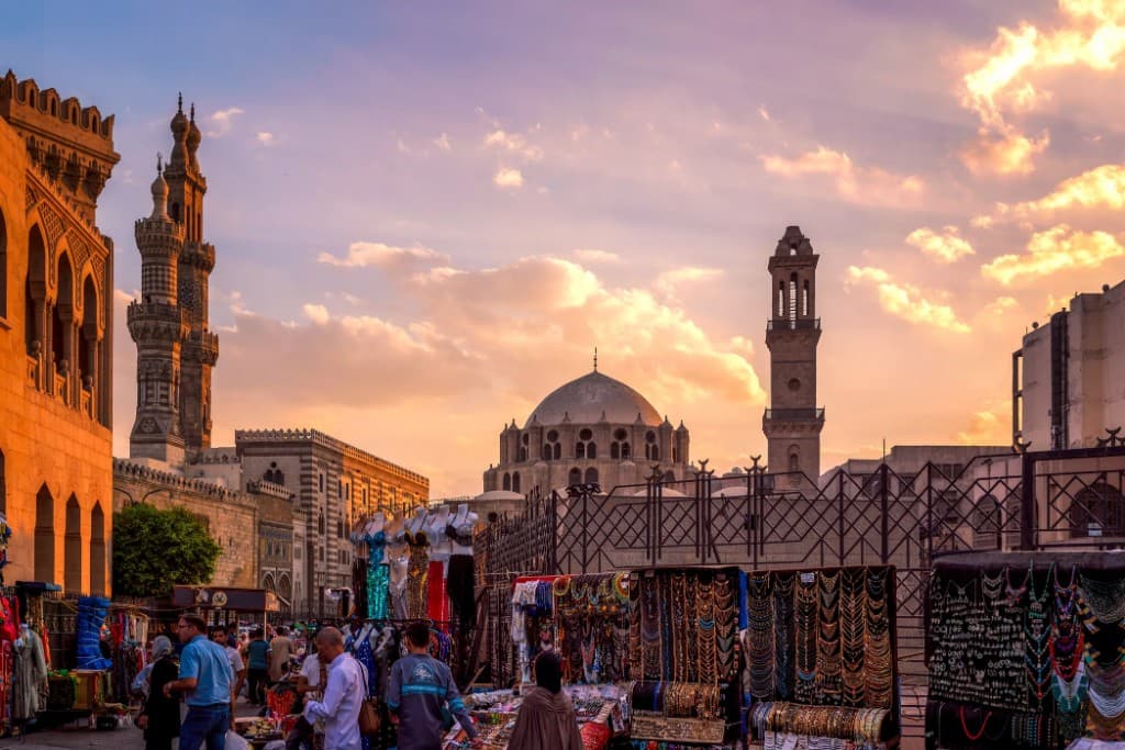 Khan el-Khalili at sunset: market stalls, Islamic dome and minarets, and visitors in the square